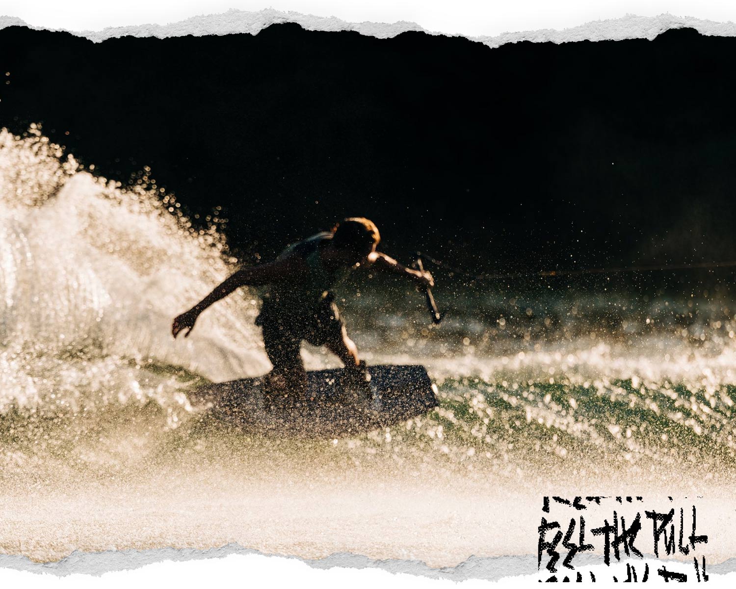 Wakeboarder carving hard with water spray lit by sunlight, silhouetted against a dark background.