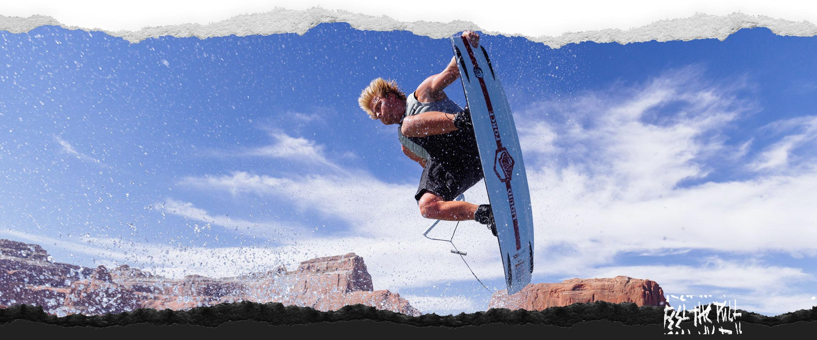 Rider performing air trick on Origin wakeboard with desert cliffs and blue sky.
