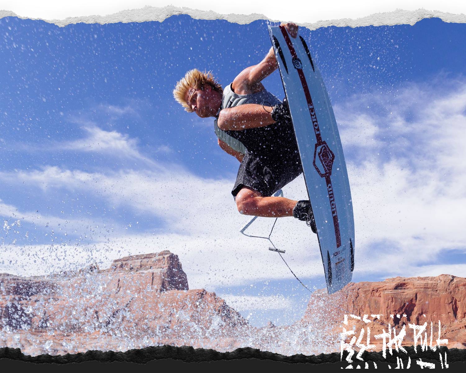 Rider performing air trick on Origin wakeboard with desert cliffs and blue sky.