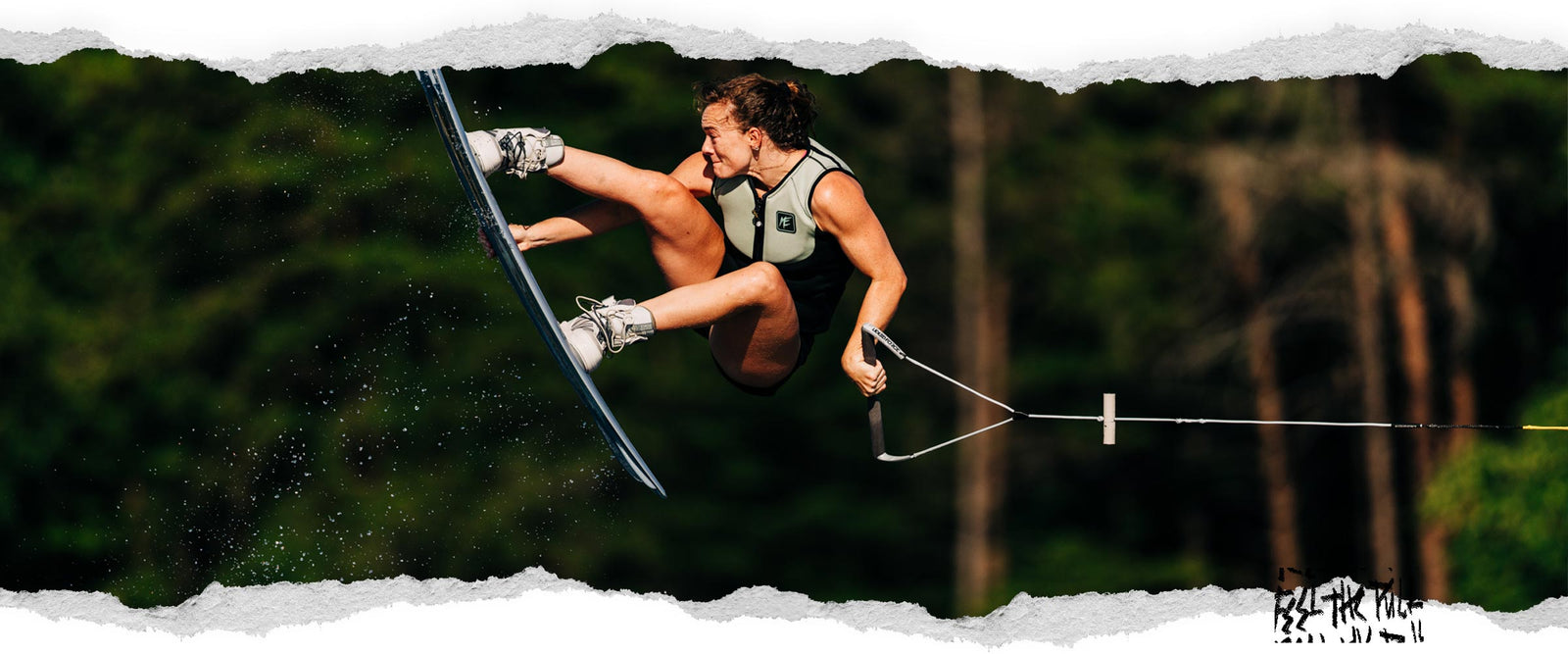 Wakeboarder in midair grab trick wearing white bindings and life vest.