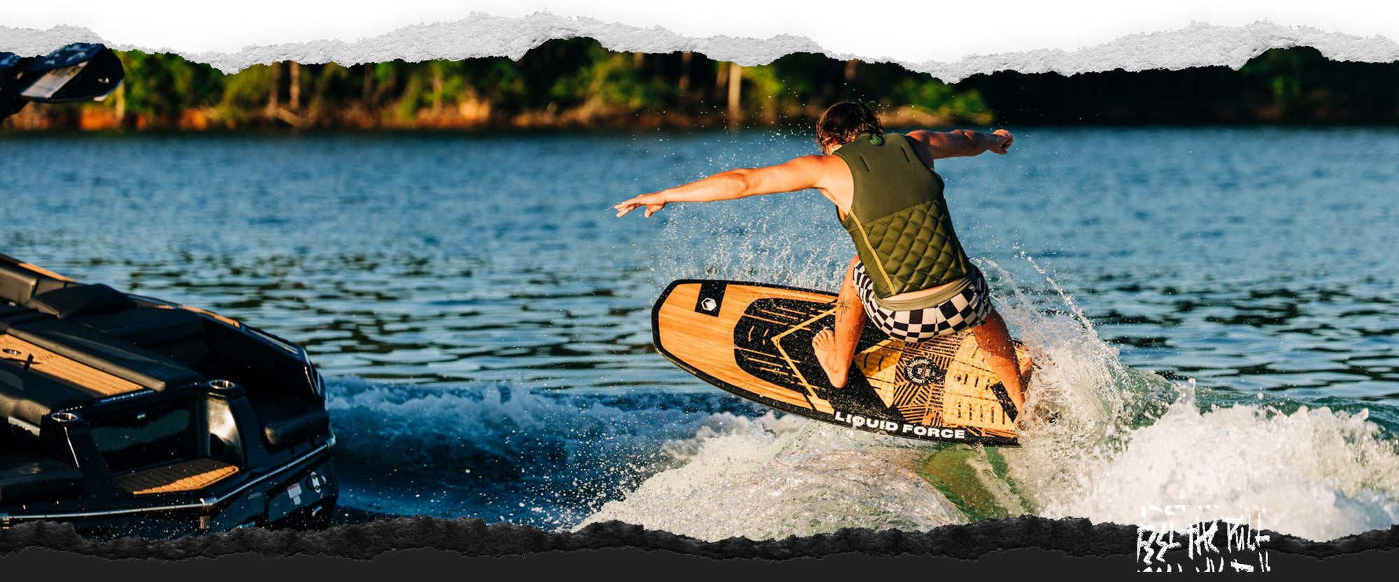 Rider in olive vest launching from boat wake on a woodgrain wakesurf board.