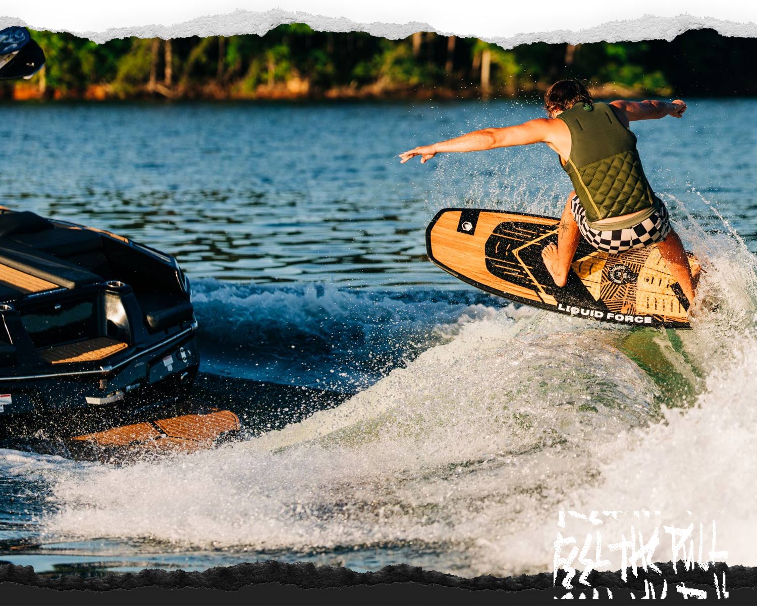Rider in olive vest launching from boat wake on a woodgrain wakesurf board.