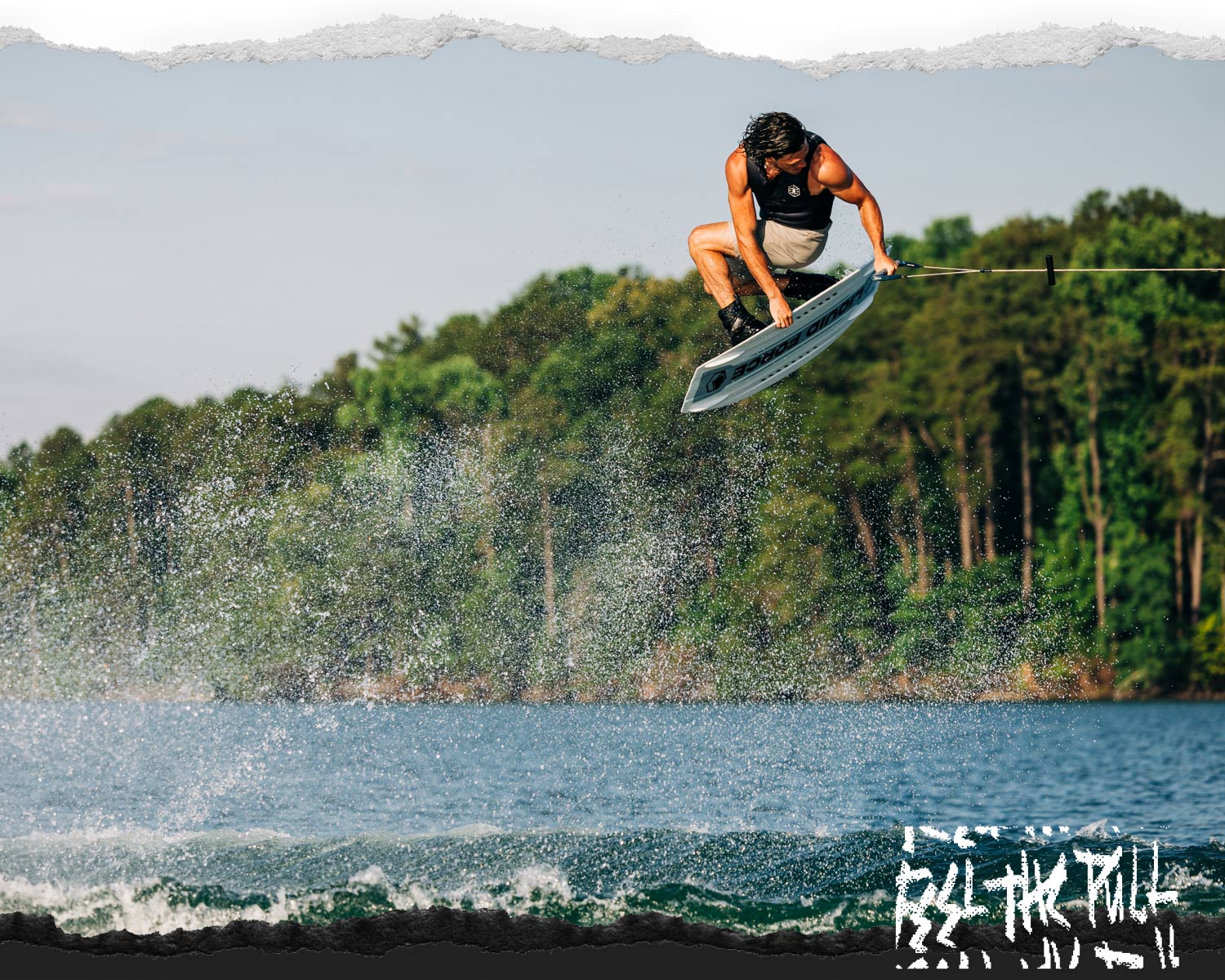 Wakeboarder grabs white Prime Aero board above water with forest in background.