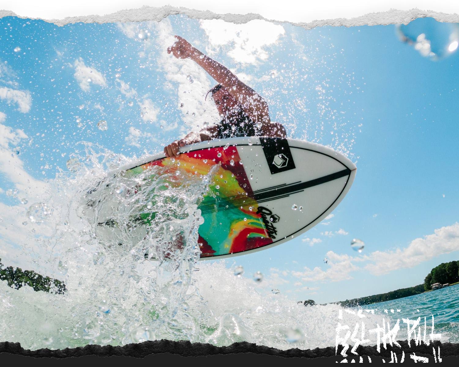 Close-up of rider in air above wake on a white wakesurf board with tie-dye bottom graphic.