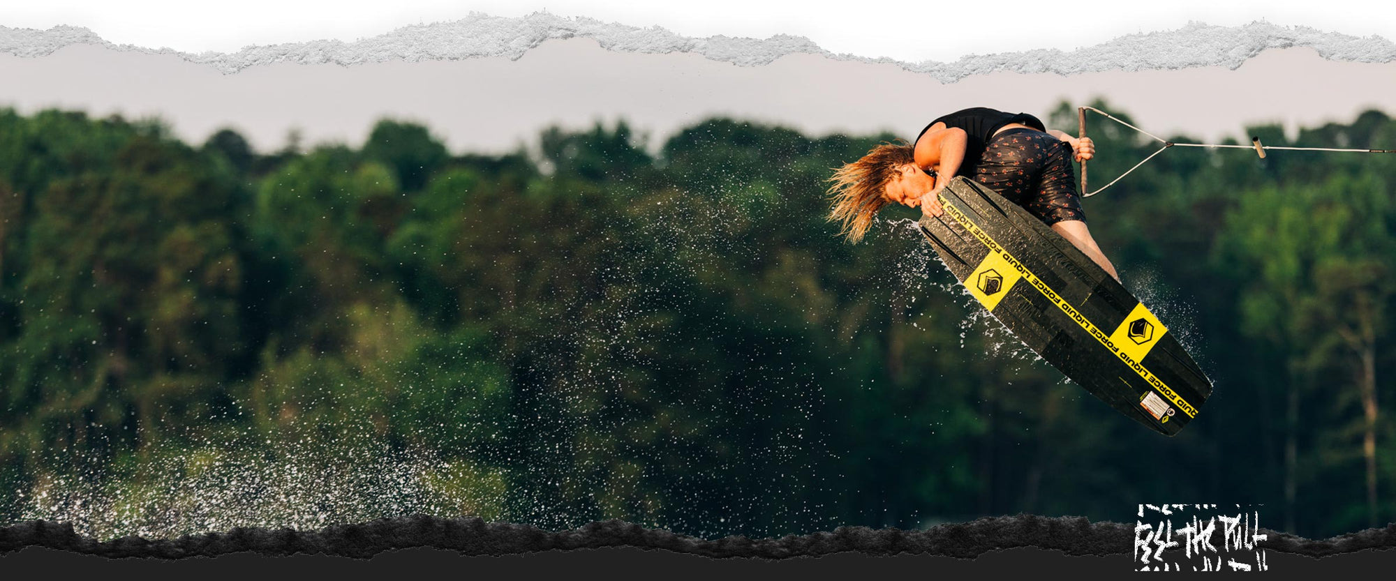 Rider launches over water on black and yellow Liquid Force wakeboard.