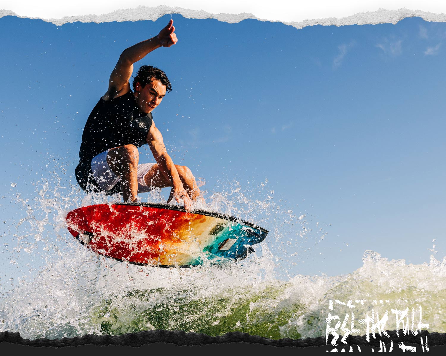 Rider launching off the wake on a multicolor wakesurf board against a clear blue sky.