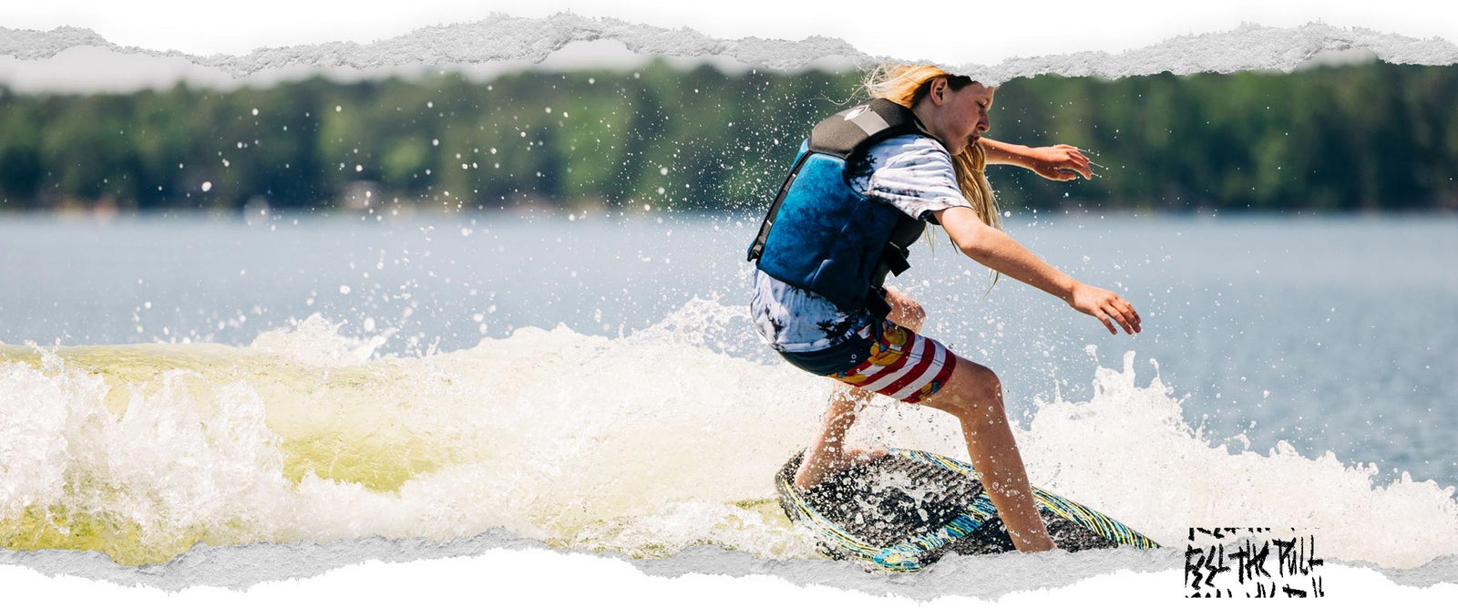Kid surfing on a black and blue wakesurf board while wearing a black Ruckus CGA vest.