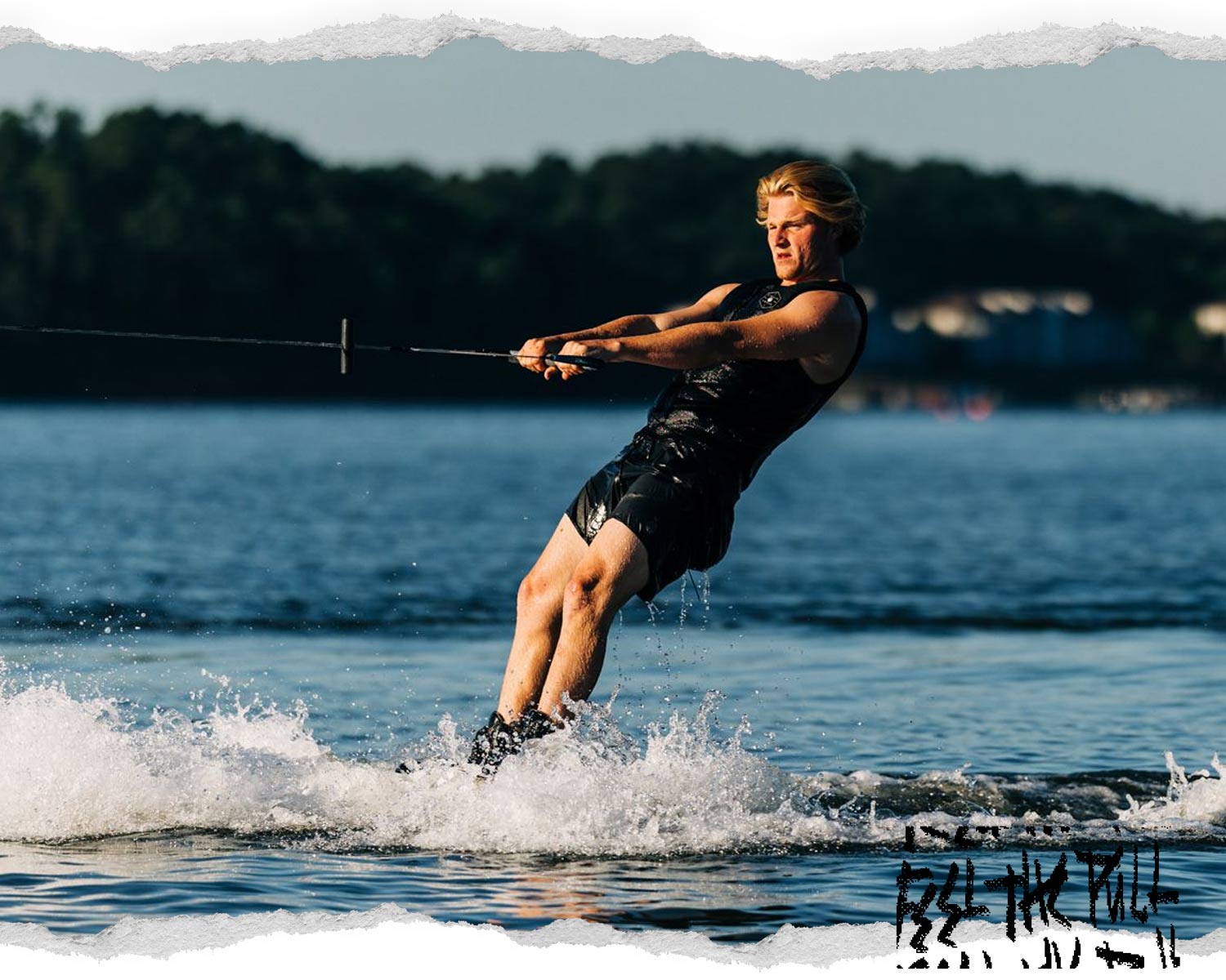 Wakeboarder skimming across water in black vest, pulling on a tow handle.
