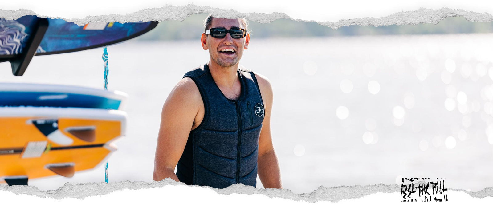 Smiling man wearing the Liquid Force Squad Comp Denim Vest on a dock.