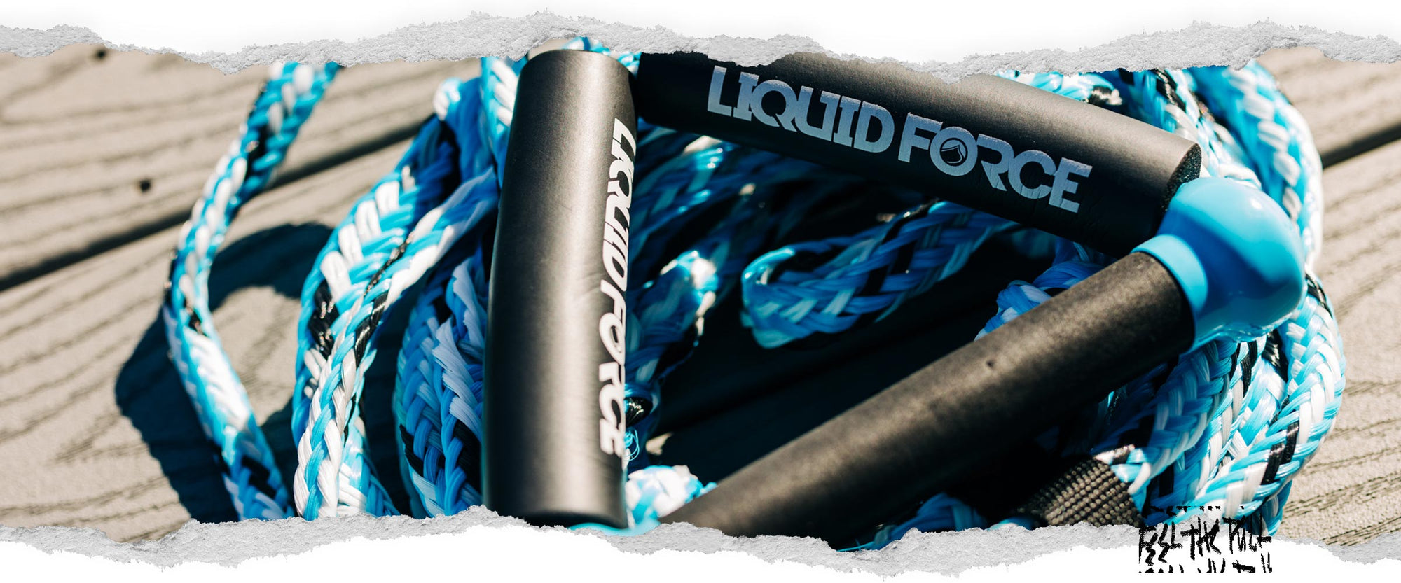 Blue and white Liquid Force handle and rope resting on wood planks.
