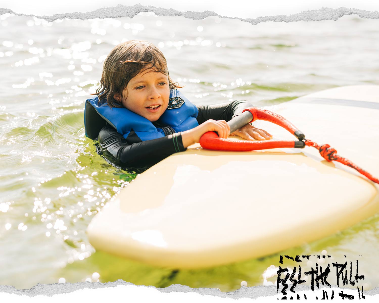Child in blue vest holds red Liquid Force handle while floating on board.
