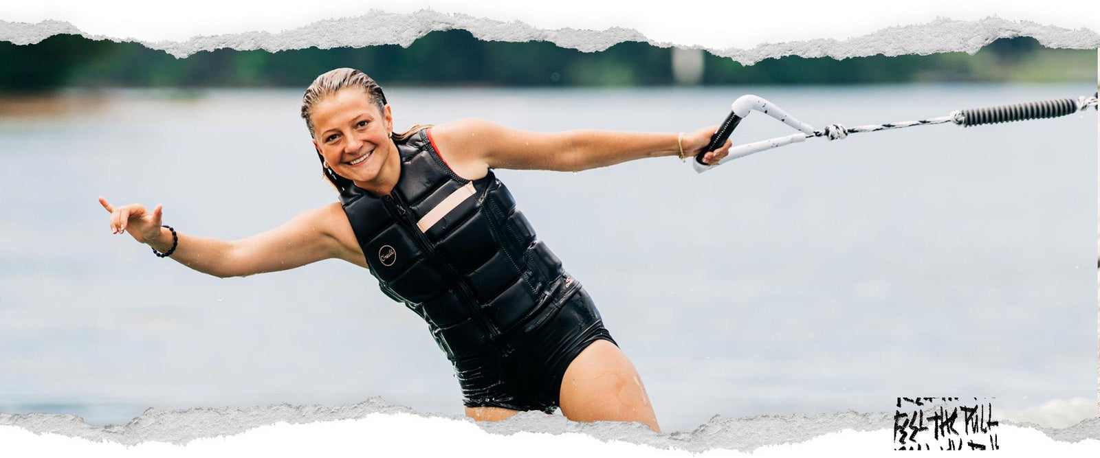 Woman in black vest wakeboarding while smiling and holding a white handle.
