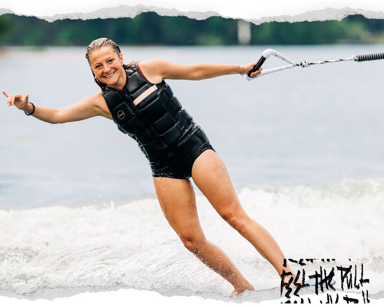 Woman in black vest wakeboarding while smiling and holding a white handle.