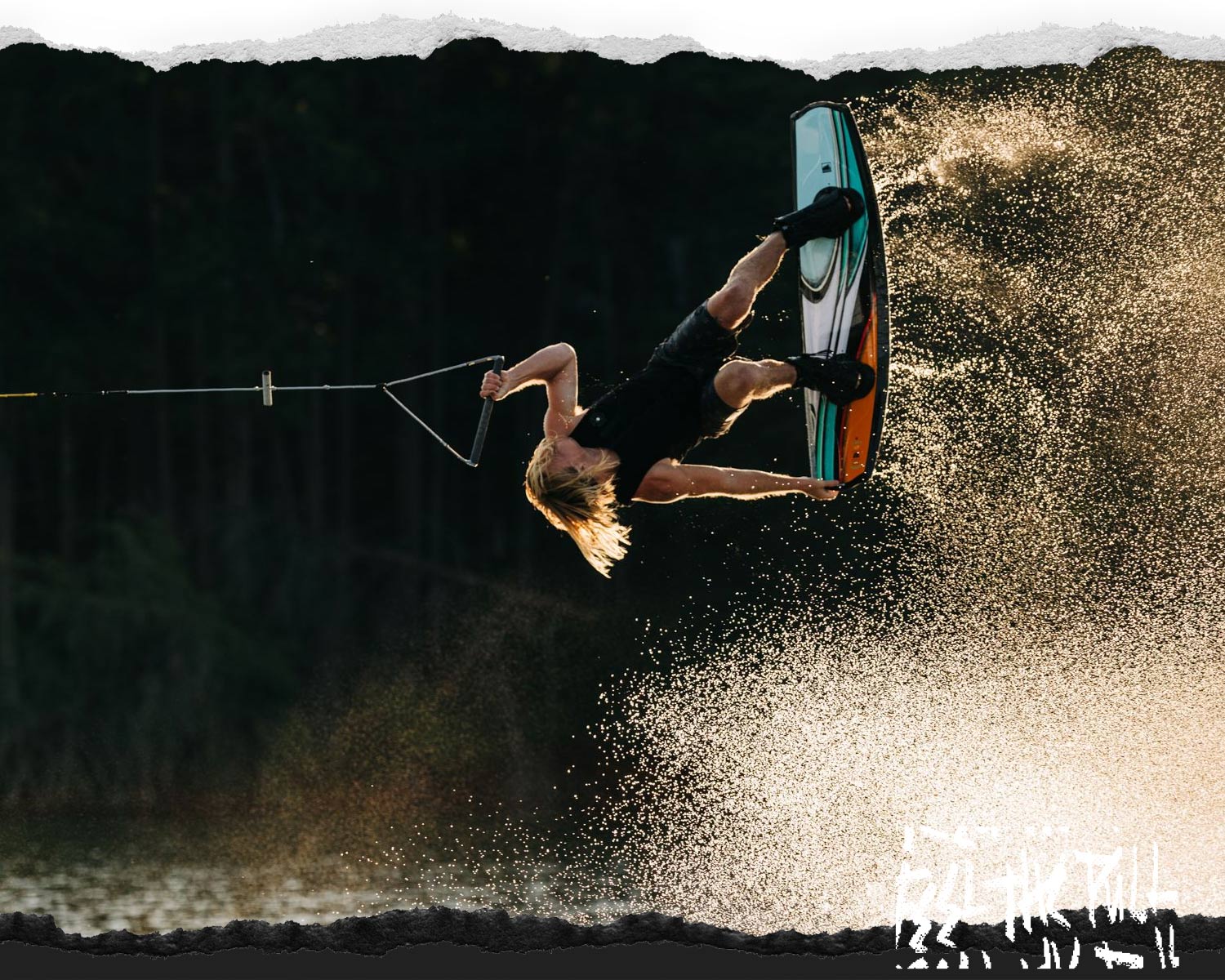 Rider doing a wakeboard flip over the water with spray lit by sunset light.