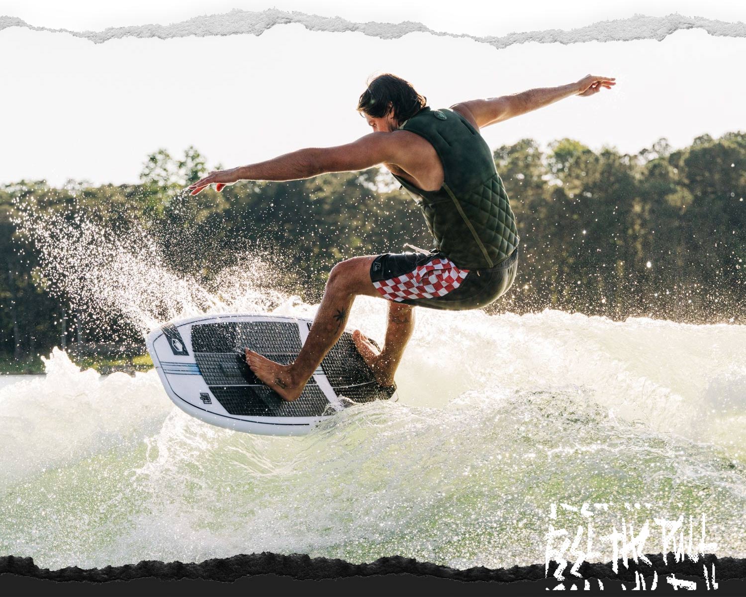 Rider in olive vest mid-turn on a white wakesurf board with dark traction pad.