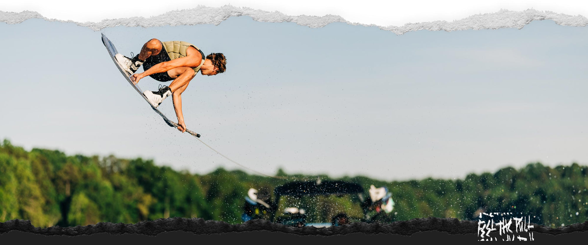 Rider airborne above boat wake on gray Unity Aero wakeboard.