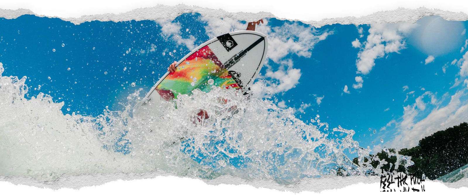 Bright surfboard with tie-dye colors carving through water against blue sky.