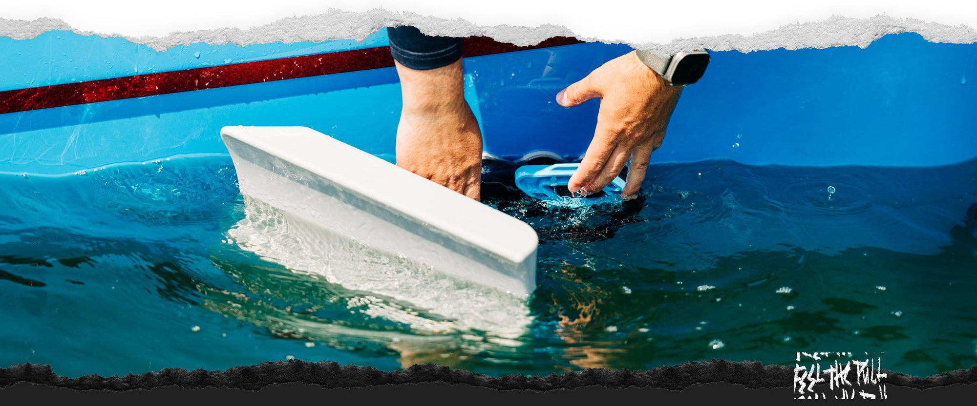 Hands attaching a Wakesurf Edge shaper to the side of a blue boat partially submerged in water.