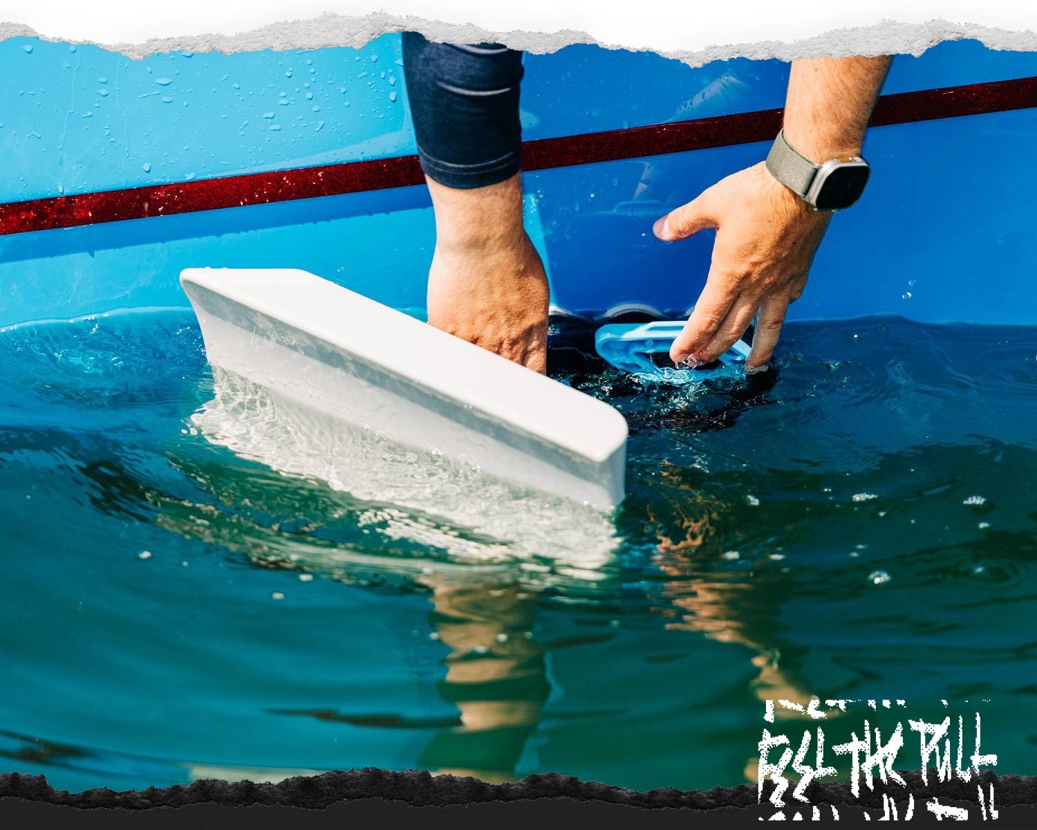 Hands attaching a Wakesurf Edge shaper to the side of a blue boat partially submerged in water.
