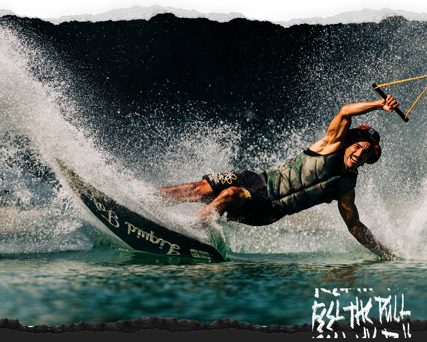 Wakeboarder carving hard on the water while holding a handle and wearing a camo vest and hat.