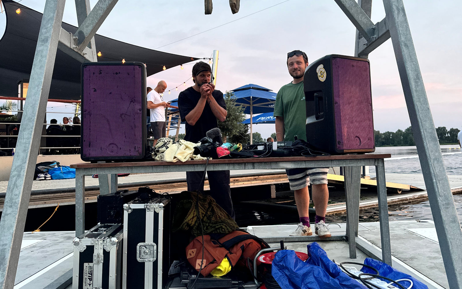 Close-up of DJ setup on dock with two men and speaker equipment in the foreground.