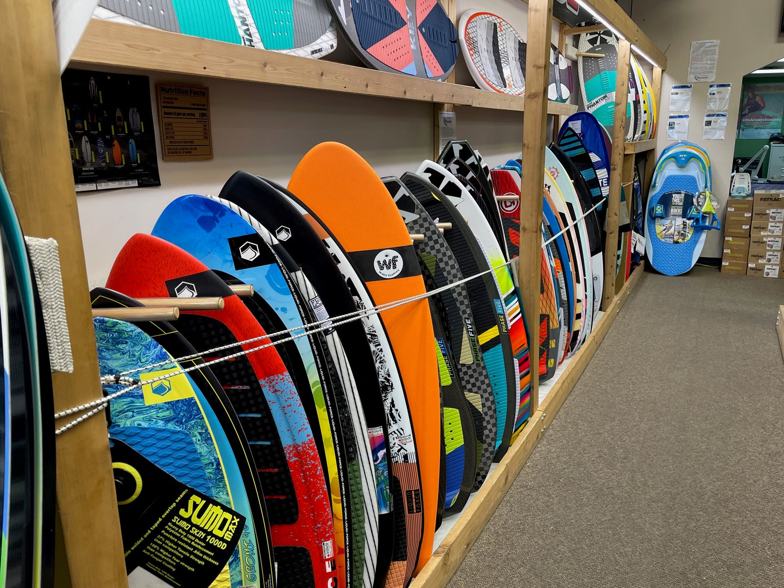 Colorful wakesurf boards lined up on display inside a wooden rack at a store.