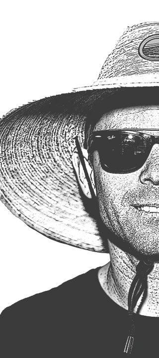 Man in a wide-brimmed hat and sunglasses, face half visible, captured in monochrome.