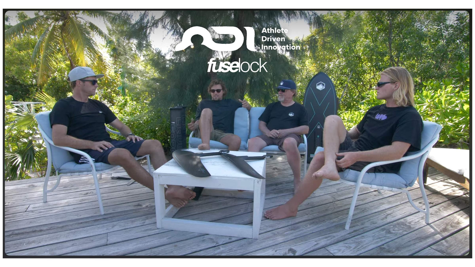 Four men sitting outdoors discussing Liquid Force foil wings with gear on table.