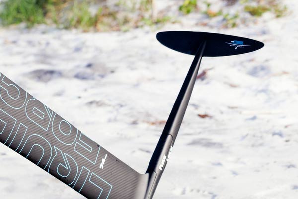 Close-up of the LiquidForce FuseLock carbon foil with thin Blue LiquidForce logo in front of a sand background.